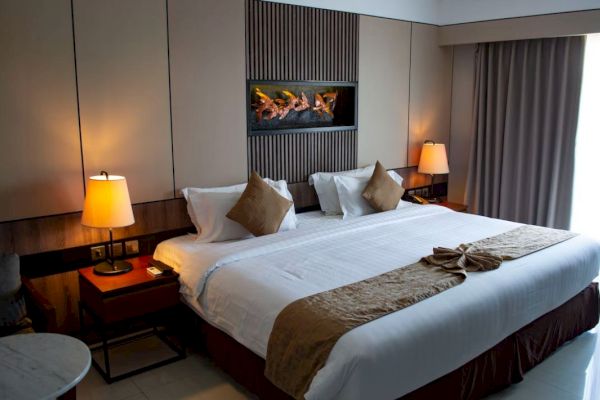 A cozy hotel room with a large bed, white linens, decorative pillows, bedside tables, lamps, and a wall-mounted artwork above the bed's headboard.