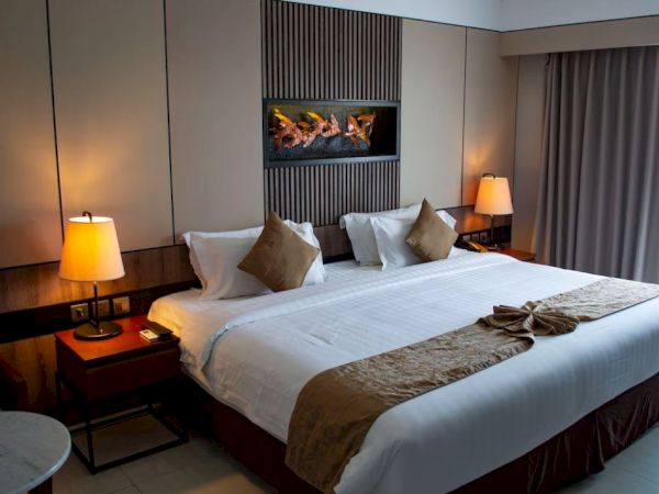 A cozy hotel room with a large bed, white linens, decorative pillows, bedside tables, lamps, and a wall-mounted artwork above the bed's headboard.