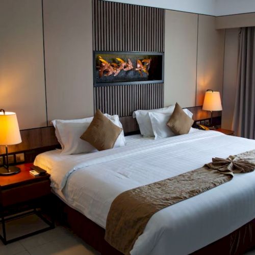 A hotel room features a neatly made king-size bed with two bedside tables, warm lighting, and a large window with curtains.