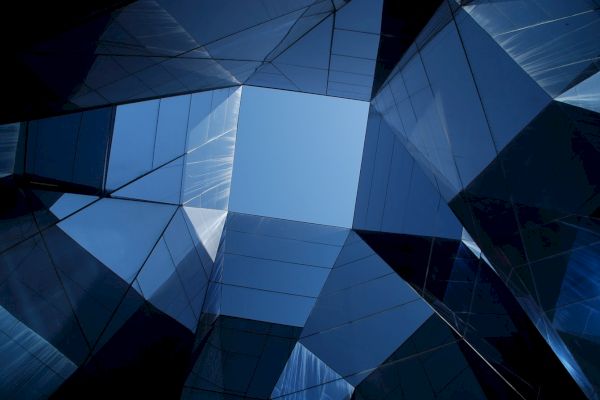 The image shows a geometric architectural structure with reflective glass panels, creating a view towards the sky through an angular, abstract opening.