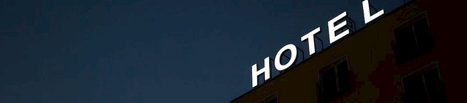 The image shows a building at night with the word "HOTEL" in illuminated letters. The "T" in "HOTEL" is partially out.