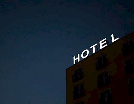 The image shows a building at night with the word "HOTEL" in illuminated letters. The "T" in "HOTEL" is partially out.