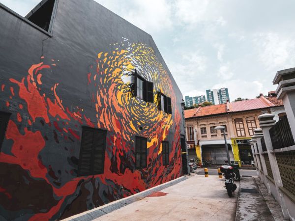 A vibrant street art mural on a building wall, depicting swirling colors, along a narrow alley with buildings, a motorcycle, and city in the background.