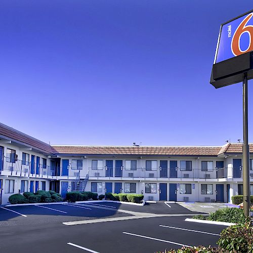 The image shows a two-story motel building with blue doors and windows, a parking lot, and a 