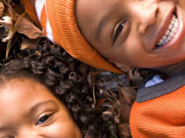 Two children lying on leaves, smiling happily, and wearing autumn-colored clothing.