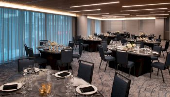 An elegantly set dining area with round tables surrounded by chairs, each table adorned with flowers, napkins, glassware, and cutlery.