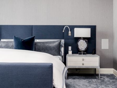 A modern bedroom with a blue and white color scheme, featuring a bed, a nightstand with a lamp, and a decorative stone element on the table.