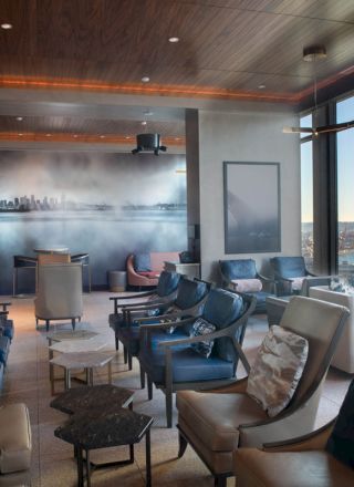 A modern, spacious lounge with comfortable seating, large windows with a scenic view, and a mural on one wall.