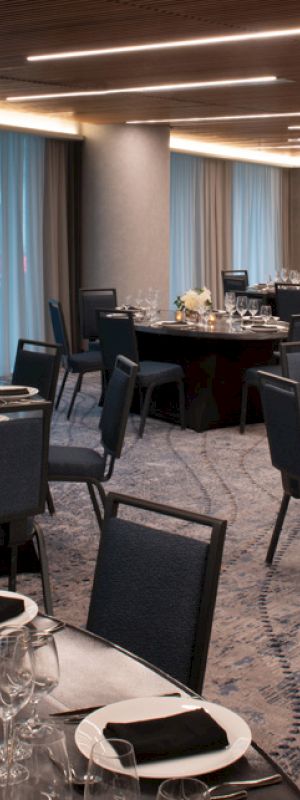 A banquet hall with round tables, black chairs, elegant table settings, candles, and floral centerpieces, ready for an event.