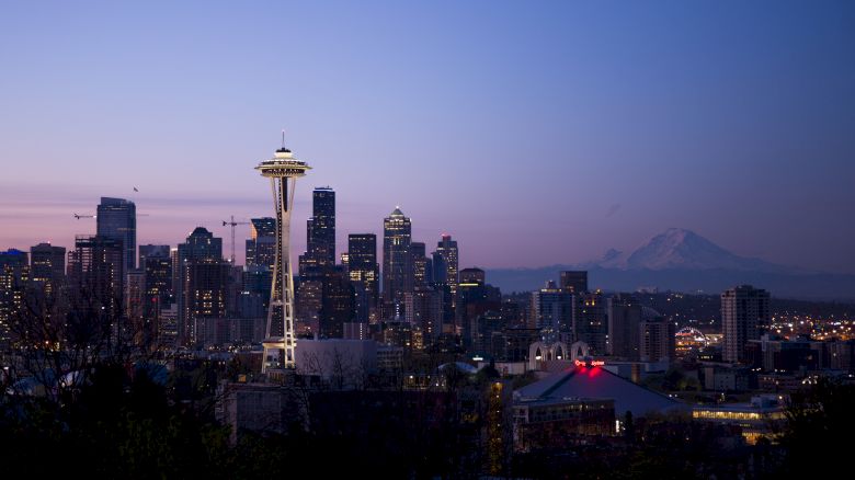 The image shows the Seattle skyline at dusk, featuring the Space Needle prominently with Mount Rainier visible in the background.
