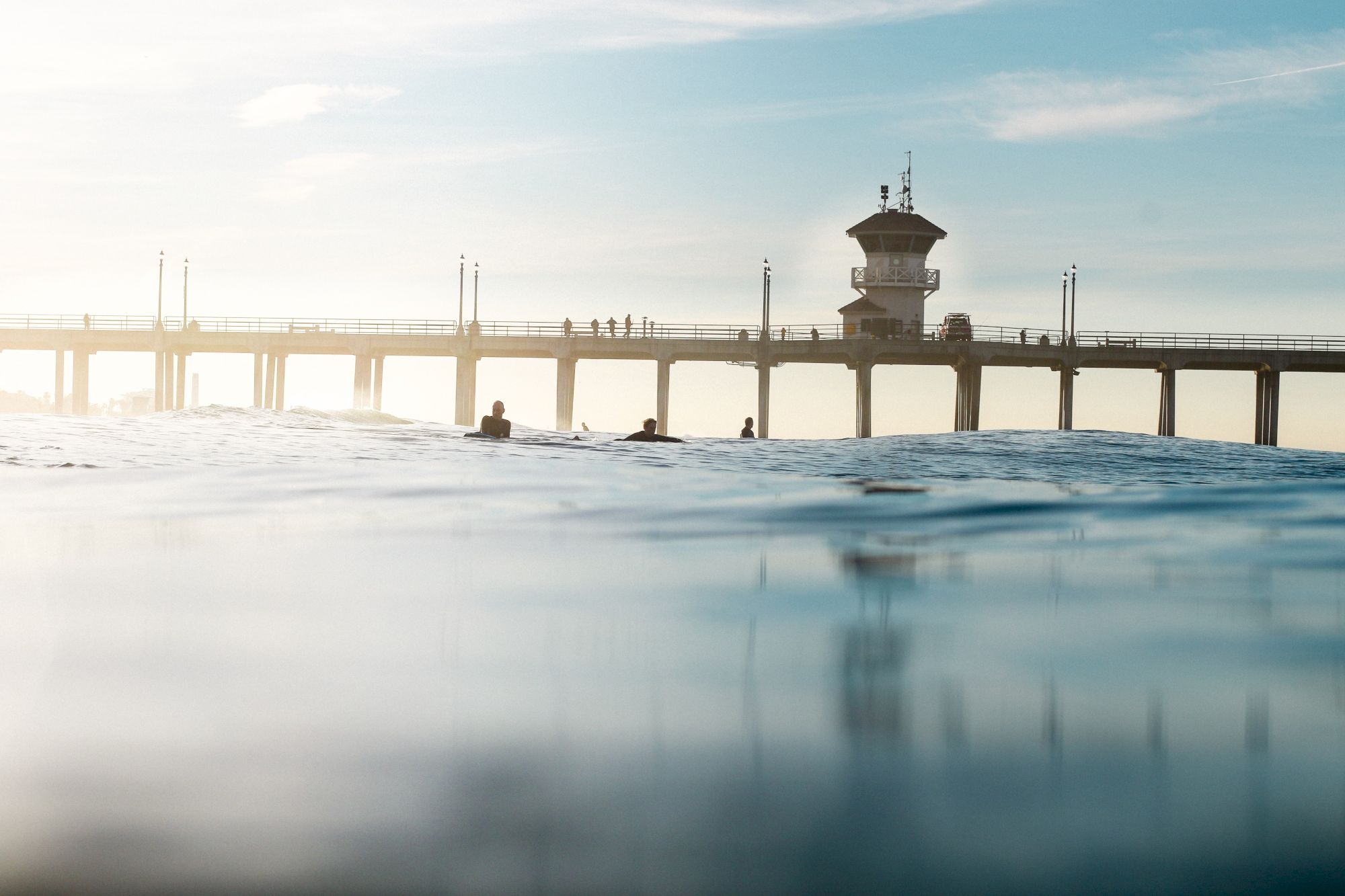 The image shows a pier extending over a calm body of water with a few people visible in the distance and a tower-like structure on the pier.